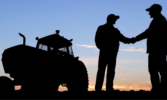 Silhouette of two men shaking hands next to a tractor